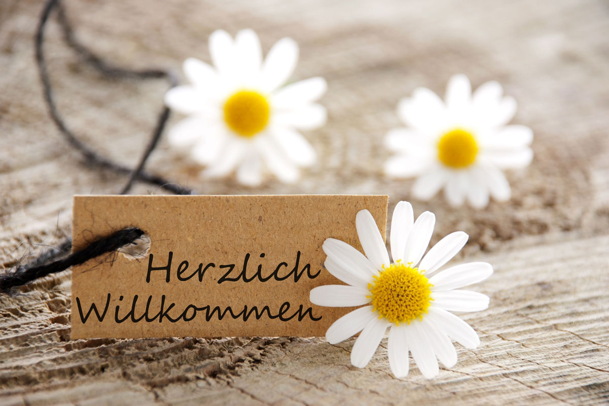 Label mit Aufschrift Herzlich Willkommen dekoriert mit weißen Blüten