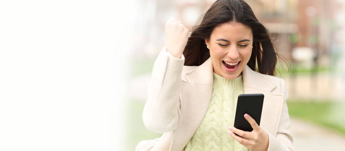 Junge Frau, die in ihr Mobiltelefon blickt und sich freut.